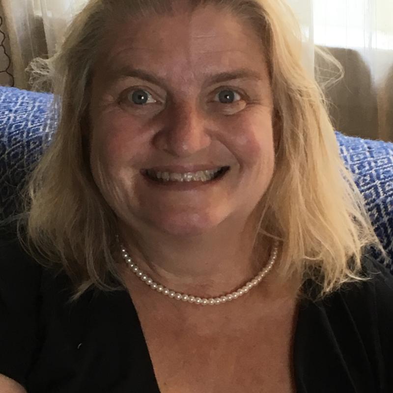 Laura Belfiglio sitting down wearing a black blouse with pearls on her neck and her hair down, smiling at the camera.