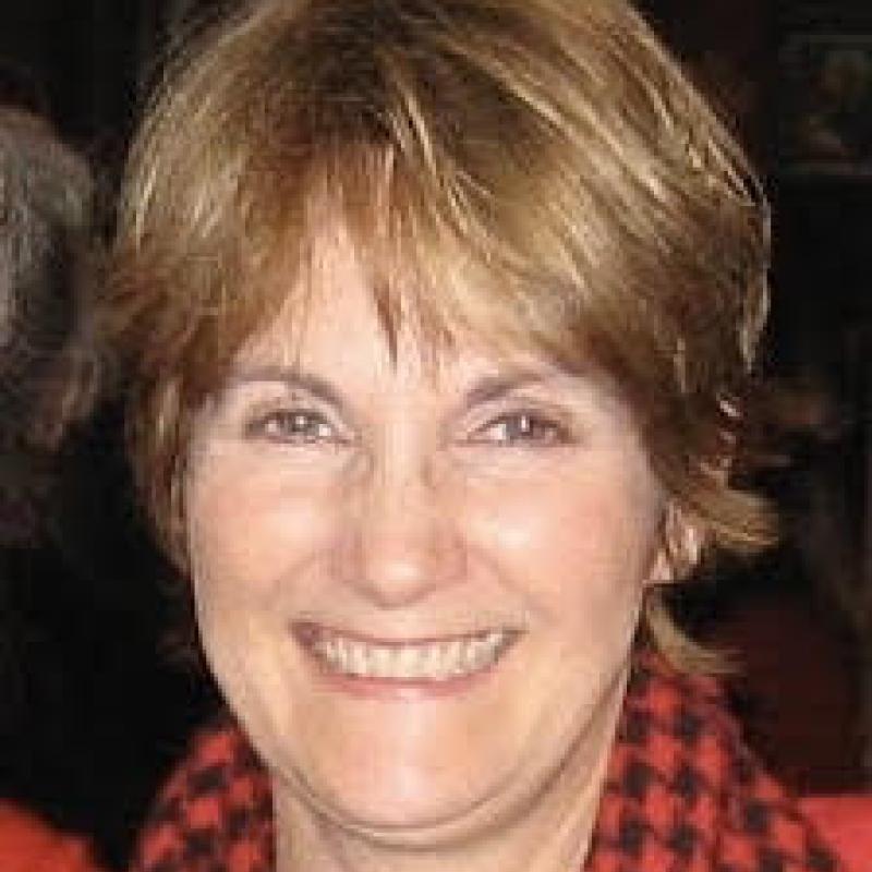 Mary Gail Stablein wearing a red and black flannel button-up with a black shirt smiling at the camera. 
