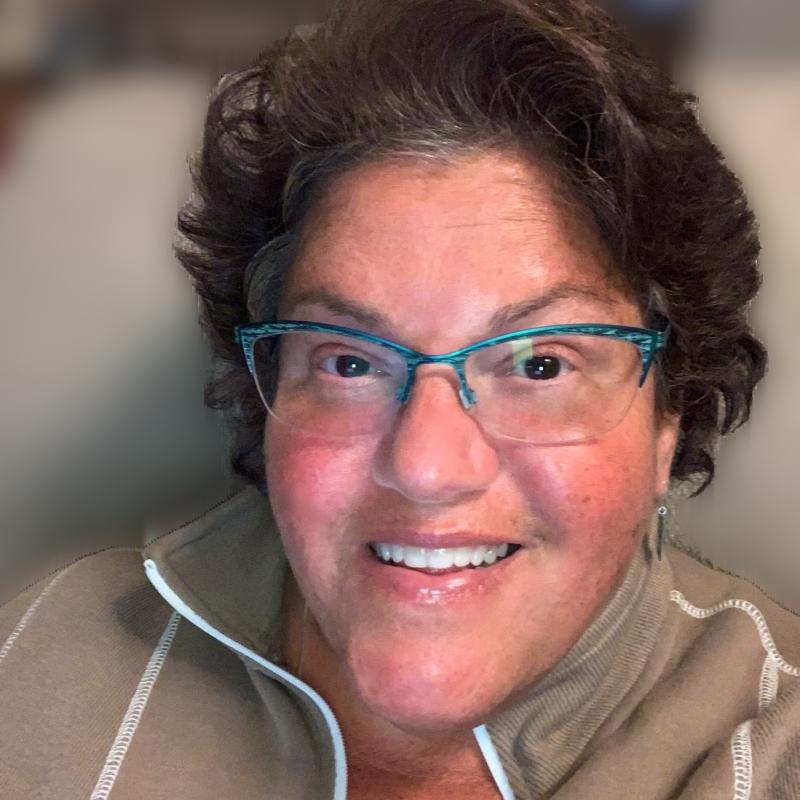 Sandy Ayala similing while wearing a zip up sweater and glasses. 